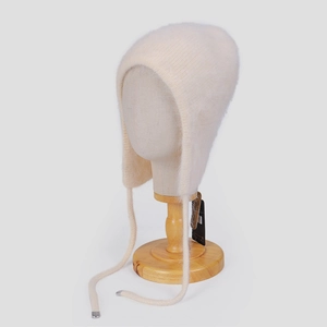 Detail einer cremefarbenen flauschigen Strickmütze mit Ohrenklappen und langen Bändern
