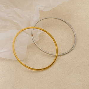 Minimalist stackable 18K gold and silver plated titanium steel bangles on textured surface
