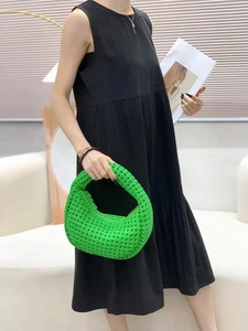 Detail of bright green woven crescent handbag held by a woman in a black dress