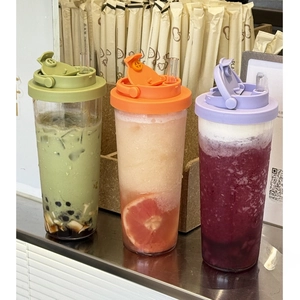 Three transparent Tritan cups with colorful lids and straws shown on a sleek metal counter