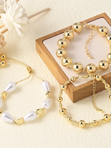 Detailed view of layered 18k gold plated bracelets with white pearls on a wooden stand