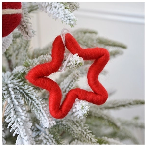Detail of a handmade red wool felt star ornament hanging on a snowy Christmas tree branch