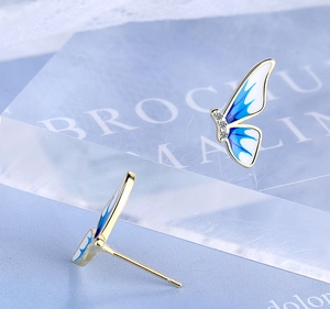 Detailed macro view of enamel butterfly stud earrings with blue gradients and gemstones