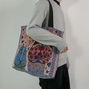 Close-up of woven tote bag with artistic cat patterns and colorful heart details