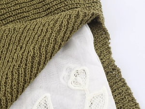 Detail of olive green knit sweater featuring white lace patchwork and heart embroidery