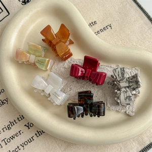 Six assorted acetate bow hair claws in tortoiseshell and marble patterns on a ceramic tray