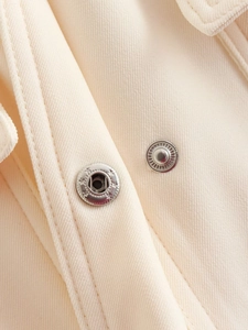 Detail shot of metallic press-stud button on high-quality beige twill fabric texture