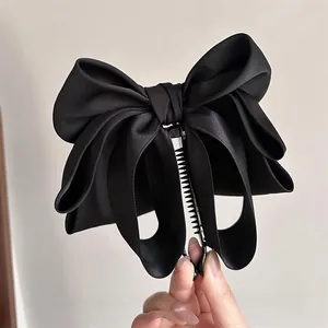 Detail of a large black satin bow banana clip with layered fabric texture for hair