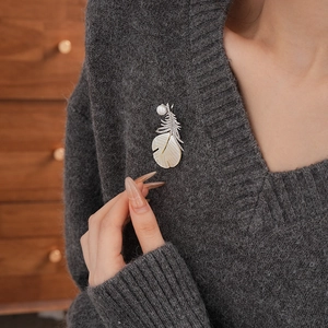Detail of elegant gold-plated feather brooch with pearl and zircon on gray sweater