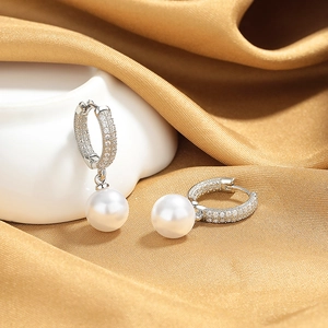 Macro shot of silver pearl drop earrings with micro-set zircon on gold silk background