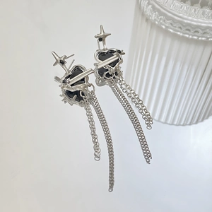 Detail of silver tassel earrings with black heart stones and star charms on white mirror
