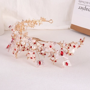Close-up of golden Baroque bridal crown with pink flowers, red crystals and butterflies