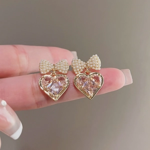 Dettaglio macro di orecchini a fiocco dorati con perle finte e gemma rosa a forma di cuore