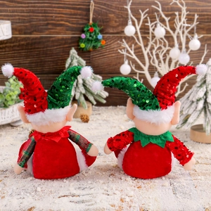Cute Christmas elf figurines with red and green sequin hats on a snowy wooden background