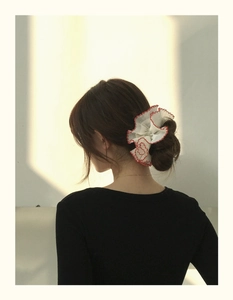 Détail d'un chouchou floral crème avec bordure en dentelle rouge sur les cheveux