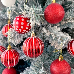 Macro shot of assorted red Christmas ball ornaments with glitter and patterns on snowy pine