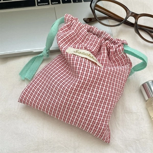 Close-up of a red gingham drawstring pouch on a desk with lifestyle accessories