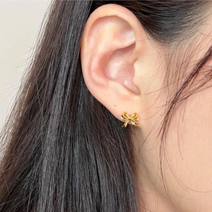 Close-up of elegant gold bow earrings worn to show the high-quality metallic luster