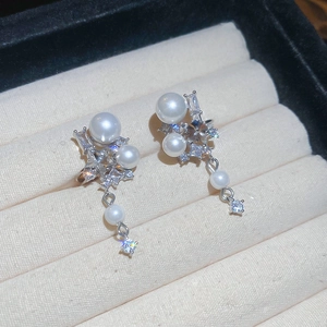 Macro detail of star-shaped zircon and pearl drop earrings on beige fabric background