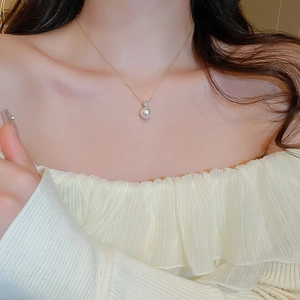 Detail of elegant gold pearl necklace with zircon pendant worn on a female collarbone