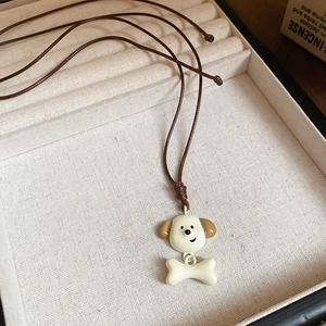Détail du pendentif chiot blanc et os sur cordon marron dans un coffret beige