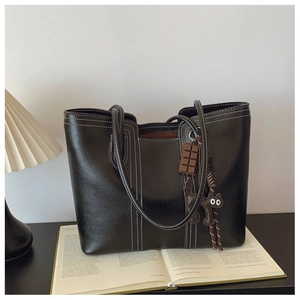Close-up of black tote bag with white stitching detail and cute cat charms on a book