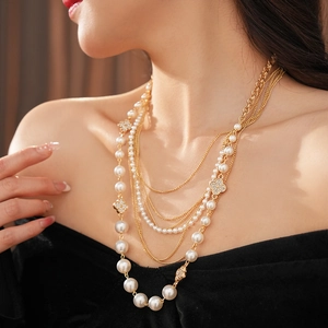 Detail of multi-layer gold chain necklace with white pearls and clover pendant