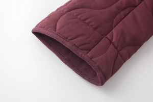 Macro detail of wine red quilted coat sleeve featuring premium curved stitching texture