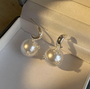 Detailaufnahme von Perlenohrringen mit silbernen Sternen in einer Satinschmuckbox