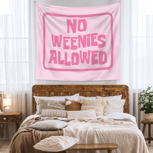 Pink bohemian tapestry with 'NO WEENIES ALLOWED' text hanging above a cozy bed