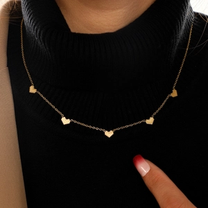Close-up of gold heart pendant necklace styled with a black turtleneck and beige blazer
