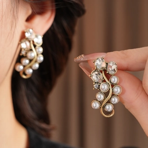 Detailed view of vintage gold earrings with white pearls and sparkling crystals on model