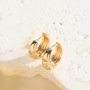 Close-up of golden earrings with sun pattern and small zircons on stone background