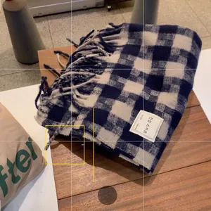 Detail view of blue and white plaid scarf with thick fringe edge and woven logo label