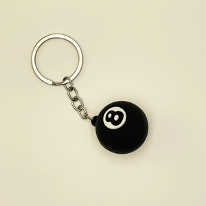 Detail view of a black 8-ball billiards keychain with a metallic ring on plain background
