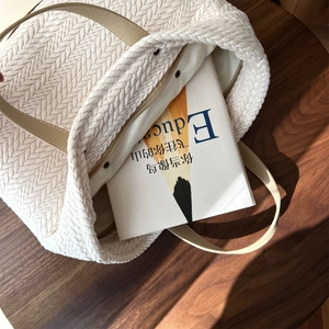 Close-up of beige woven tote bag with V-shaped texture and leather handles on wood