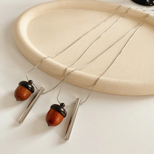 Detail view of two wooden acorn and metal bar pendants on silver chains in a beige tray