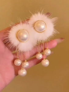 Détail de boucles d'oreilles perles avec pompons en fourrure blanche et glands dorés
