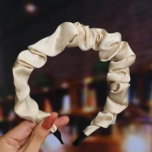 Detail of beige pleated satin headband showing rich fabric texture and smooth glossy finish
