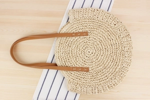 Detailed close-up of natural paper rope weave and brown leather handles on round beach bag