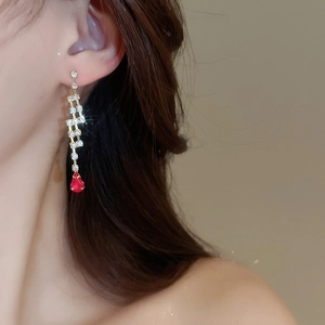 Detail of golden drop earrings with clear gems and a large red teardrop stone