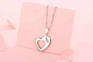 Detailed view of silver heart-shaped pendant with three diamonds on pink background