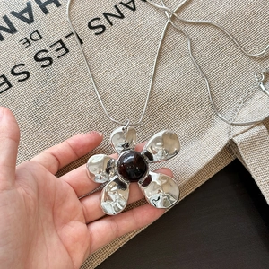 Silver flower pendant necklace with dark resin gemstone center held in hand