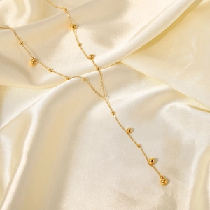 Detail view of 18K gold plated Y-shaped necklace with gold beads on satin fabric.