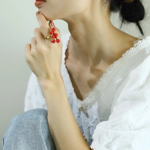 Detailed close-up of a 18k gold branch ring with five red berry beads on finger