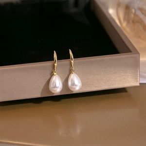 Elegant gold drop earrings with white teardrop pearls on a gray jewelry box edge