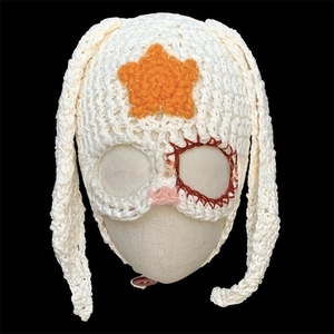 Detail of white handmade crochet knit rabbit ear hat with orange star and red stitch accents
