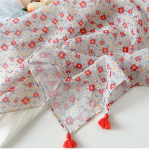 Detail of light blue floral cotton scarf featuring red tassels and soft texture