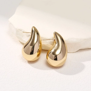 Macro shot of polished gold water drop stud earrings resting on a white textured stone