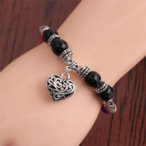 Beaded bracelet with black stones and a silver heart charm on a wrist over a wood background